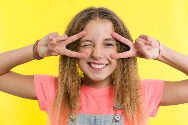 Gelukkig tienermeisje gebaren, die betrekking hebben op één oog, heldere gele studio achtergrond — Stockfoto