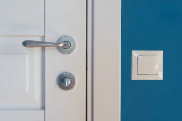 Elementi di primo piano dell'interno dell'appartamento. Dettaglio di una porta interna bianca con maniglia e chiavistello cromati, interruttore luminoso a parete — Foto Stock