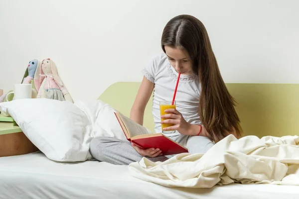 Seorang gadis remaja berusia 10 tahun dengan pakaian rumah membaca sebuah buku di tempat tidur di kamarnya — Stok Foto