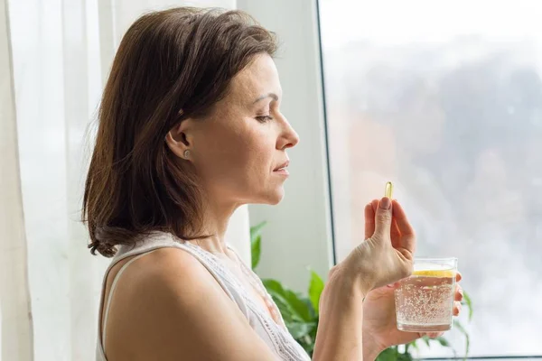 Mujer toma píldora con omega-3 y sosteniendo un vaso de agua dulce con limón . — Foto de Stock