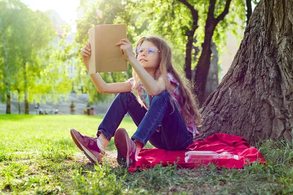 Fille enfant dans des lunettes livre de lecture dans le parc — Photo