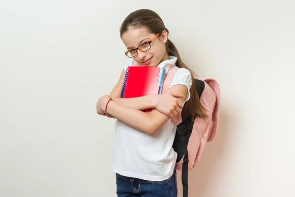 Retrato de una colegiala sonriente de 10 años con gafas, con mochila, cuadernos. fondo brillante pared en la escuela . — Foto de Stock
