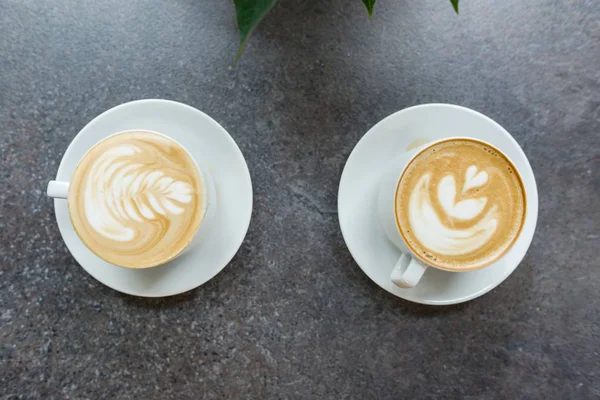 灰色の石のカウンターの上にコーヒーアートの2つの白いカップ — ストック写真
