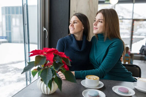 Två skrattande omfamnande unga kvinnor som sitter vid bordet på kaféet — Stockfoto