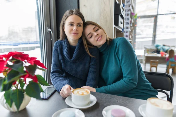 Två skrattande omfamnande unga kvinnor som sitter vid bordet på kaféet — Stockfoto