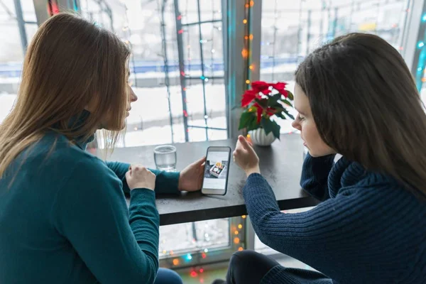 Winter portrait of talking young women sitting in cafe with mobile phone — Stock Photo, Image