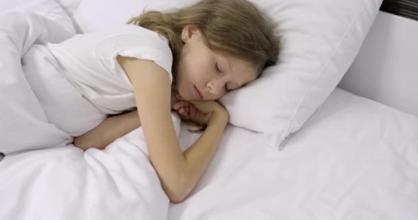 Fille enfant de dix ans avec de longs cheveux blonds bouclés dormant dans un lit blanc sur un oreiller — Video