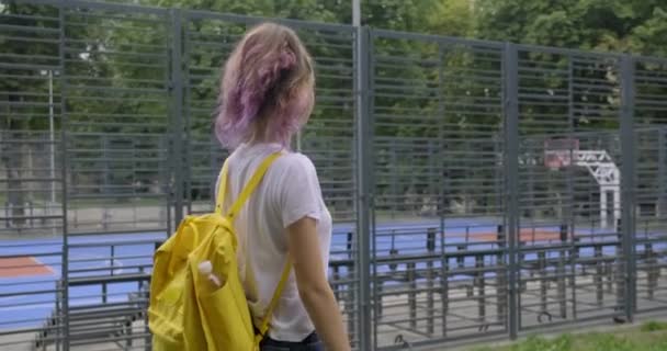 Flicka tonåring, student av 15 år promenader nära street basketplan — Stockvideo