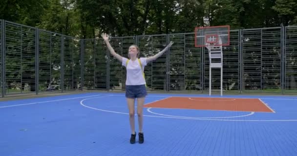 Aktivní úsměv dospívající dívka, módní s fialovými vlasy, skákání na ulici basketbalové hřiště s rukama zvednutýma — Stock video