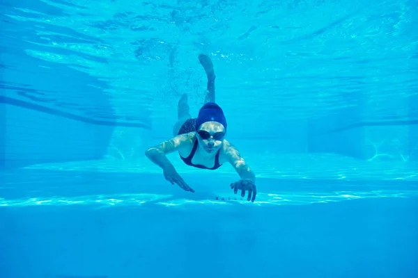 Nastolatka w stroju kąpielowym z okularami i czepkiem kąpielowym pływającym pod wodą w basenie — Zdjęcie stockowe