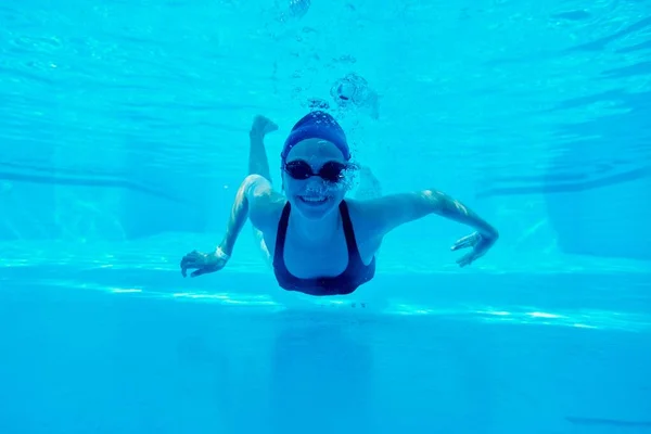 Mladá dívka plave pod vodou v bazénu, žena vypadá a usmívá se — Stock fotografie