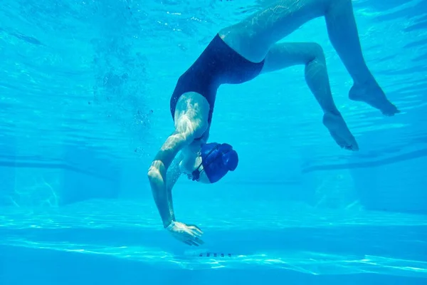 Young girl swimmer in swimsuit with goggles and swimming cap underwater in pool — Stock Photo, Image