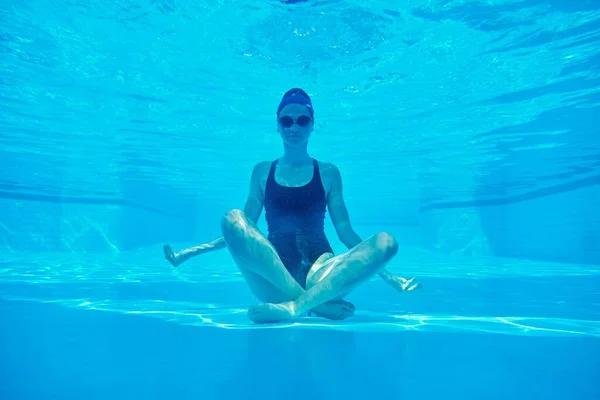 Młoda atletyczna kobieta siedząca w lotosu pozuje pod wodą w basenie — Zdjęcie stockowe