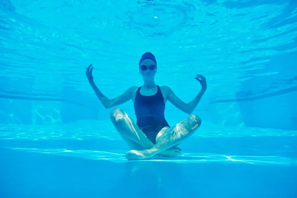 Jonge atletische vrouw zitten in lotus poseren onder water in het zwembad — Stockfoto