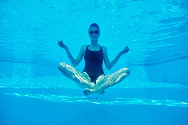 Jonge atletische vrouw zitten in lotus poseren onder water in het zwembad — Stockfoto