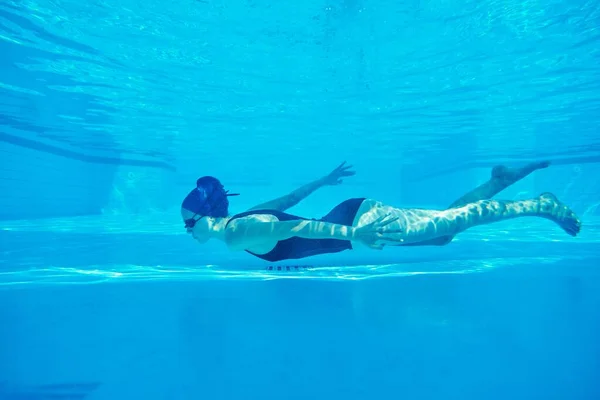 Jeune fille nageuse en maillot de bain avec lunettes et bonnet de bain sous-marin dans la piscine — Photo