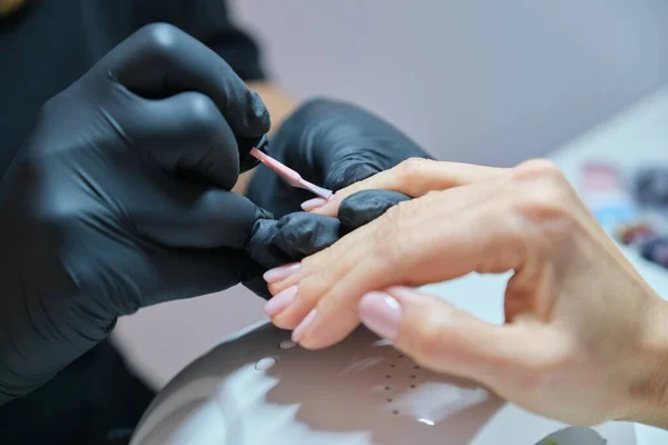 マニキュリストはジェルネイルをニスでニスを塗ります。美容室での専門的な手と爪のケア — ストック写真