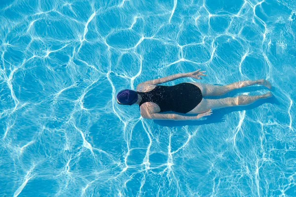 Mujer joven en traje de baño deportivo gorra nadando bajo el agua en la piscina azul al aire libre — Foto de Stock