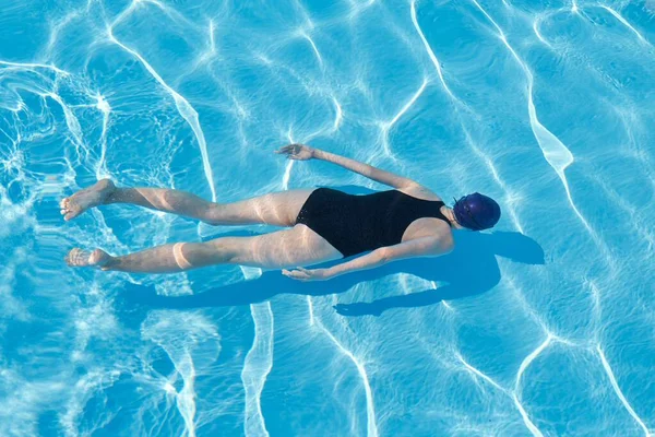 Mujer joven en traje de baño deportivo gorra nadando bajo el agua en la piscina azul al aire libre —  Fotos de Stock