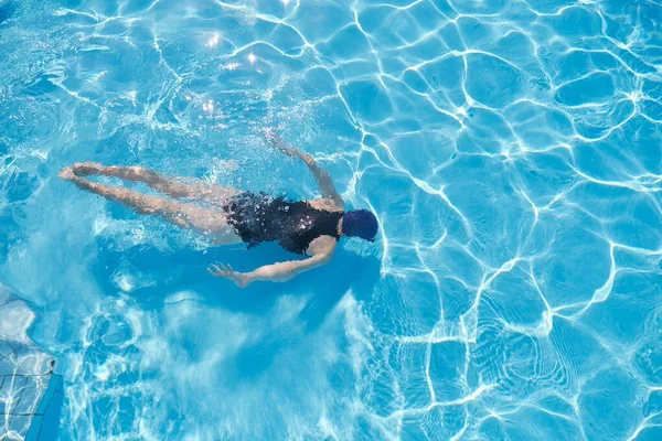Νεαρή γυναίκα κολυμπά κάτω από το νερό σε μια εξωτερική πισίνα, πάνω άποψη της πλάτης του κοριτσιού — Φωτογραφία Αρχείου