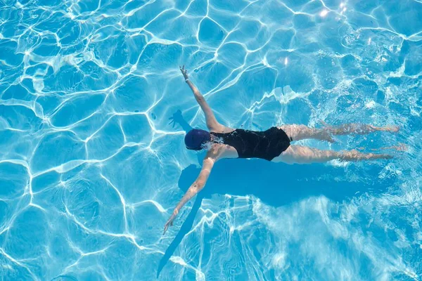 Young woman swimming underwater in an outdoor pool, top view of back of girl — Stock Photo, Image