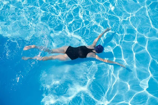 Young woman swimming underwater in an outdoor pool, top view of back of girl — Stock Photo, Image