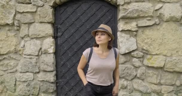 Woman tourist in hat with backpack walking from metal ancient door of medieval stone castle — Stock Video