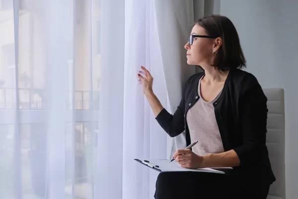 Volwassen vrouw maatschappelijk werker, psycholoog zitten in de buurt van het raam met klembord — Stockfoto