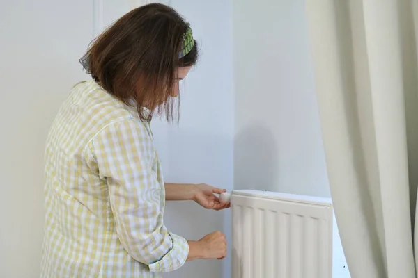 Mujer cerca de radiador de calefacción, regula la temperatura con regulador de termostato —  Fotos de Stock