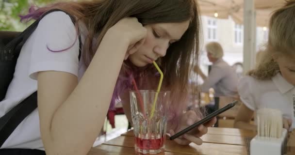 10代の女の子とともに妹座っていますでザ屋外カフェ飲料ジュースと使用スマートフォン — ストック動画