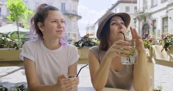 Madre e hija de 15 años sentadas en la cafetería al aire libre de la ciudad hablando y bebiendo bebidas — Vídeos de Stock