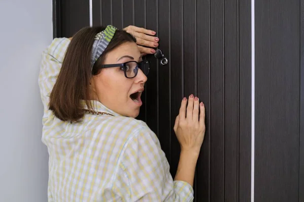 Mujer parada cerca de la puerta principal mirando a través de la mirilla — Foto de Stock