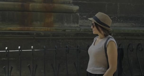 Sonriente mujer de mediana edad turista en sombrero con mochila caminando cerca de la pared de piedra del castillo medieval — Vídeo de stock