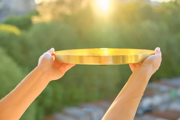 Bandeja redonda de metal de latón dorado en manos de mujeres, puesta de sol de fondo —  Fotos de Stock