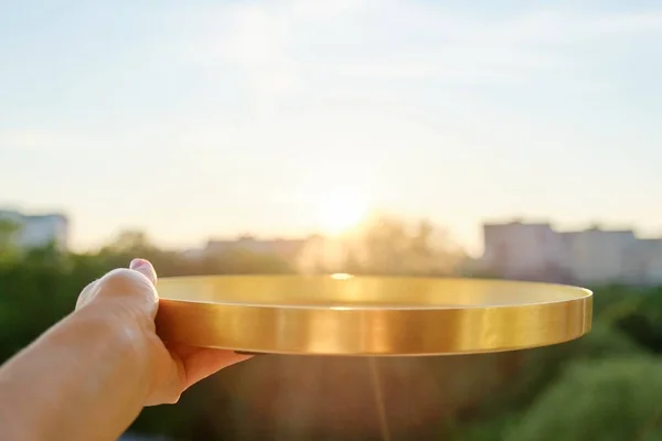 Круглый золотой металлический поднос в женских руках, фон заката — стоковое фото
