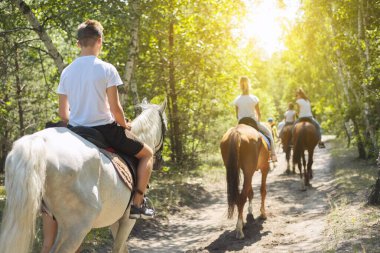Group of teenagers on horseback riding in summer park clipart