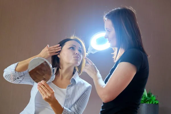 Middle-aged woman in beauty salon, talking to a beautician and looking at mirror