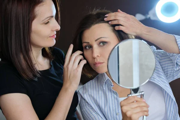 Volwassen vrouwelijke patiënt kijken in de spiegel en vrouwelijke schoonheidsspecialiste tonen op gezicht — Stockfoto