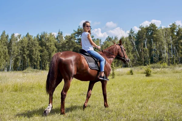 Adolescente menina montando um cavalo marrom, cavalgando para as pessoas no parque — Fotografia de Stock