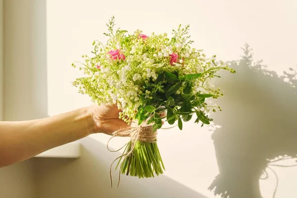 Vacker frisk bukett av liljekonvalj blommor, rosa ros, gröna grenar i kvinnlig hand — Stockfoto