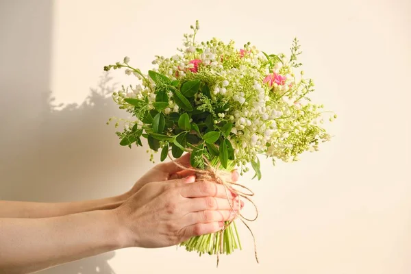 Vacker frisk bukett av liljekonvalj blommor, rosa ros, gröna grenar i kvinnlig hand — Stockfoto