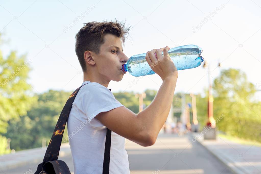 Teenager boy drinking bottle water, hot summer day