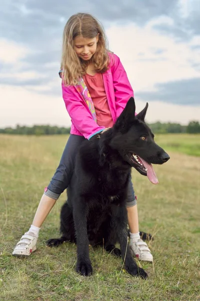 Dziewczyna przytulanie Duży czarny pies pasterz, dziecko i zwierzę spaceruje w przyrodzie — Zdjęcie stockowe