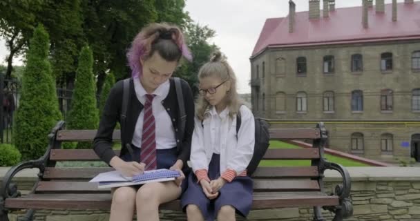 Dos colegialas sentadas en el banco, estudiante de primaria y secundaria . — Vídeos de Stock