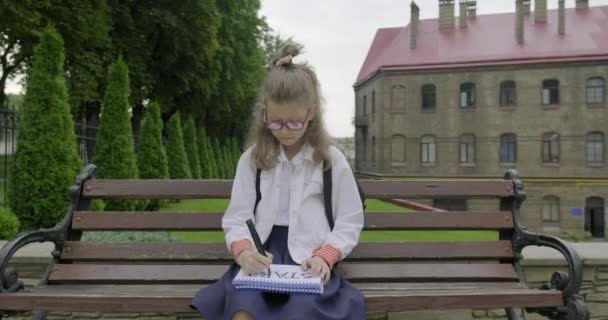 Девочка младшая школьница в очках в школьной форме пишет слово старт — стоковое видео