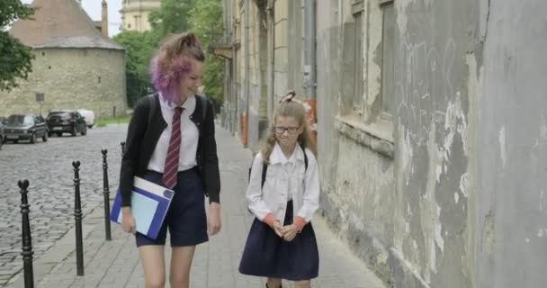 Две девочки-сестры идут в школу, дети в школьной форме с рюкзаками говорят — стоковое видео