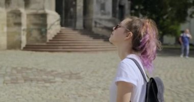 Güzel, gülümseyen, sırt çantalı genç bir kız eski bir turistik şehirde yürüyor.