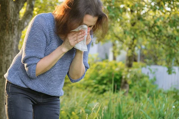 Зрелая женщина чихает в носовой платок, аллергия на пыльцу, простуда — стоковое фото