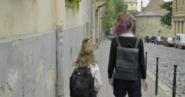 İki kız kardeş sırt çantalarıyla okula gidiyor.