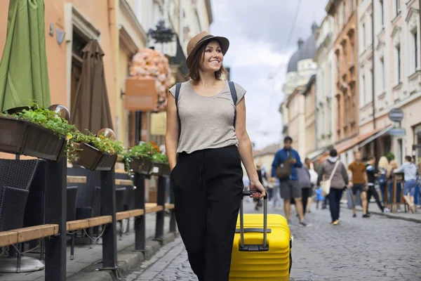 Viajando sonriente mujer madura turista en sombrero con mochila y maleta caminando — Foto de Stock